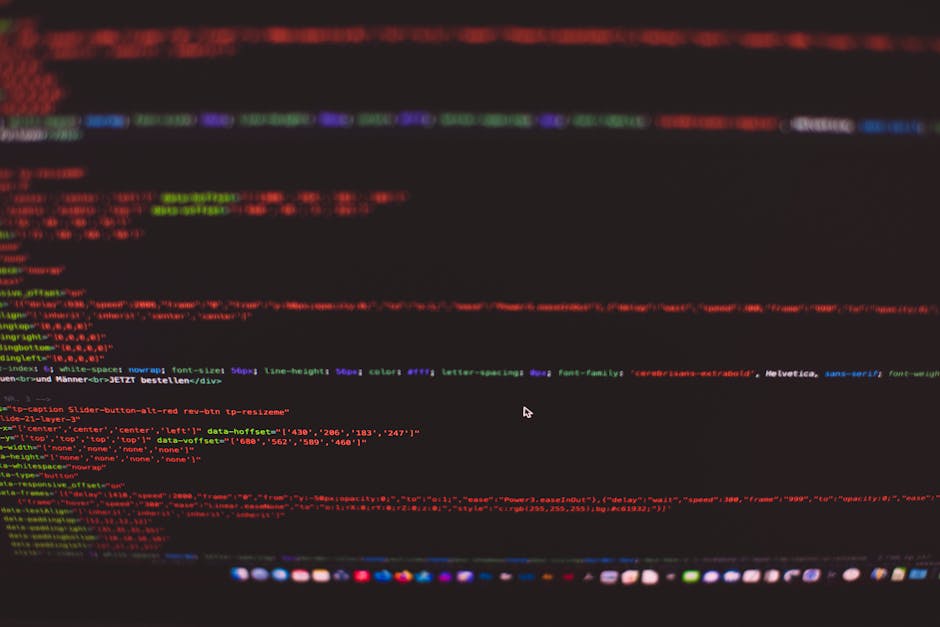 A close-up photograph of a computer screen displaying lines of multicoloured code in red, green, blue, purple, and yellow characters against a dark background. The text appears to be HTML or programmi